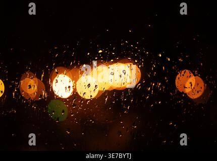 Rain drop on window at night. Outside window is blurred bokeh of raining city light Stock Photo