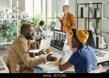 Serious Black male programmers discussing software together while sitting at desk working together in office Stock Photo