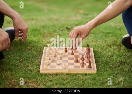 Hands of Asian father and son playing chess together sitting on grass outdoors during daytime Stock Photo