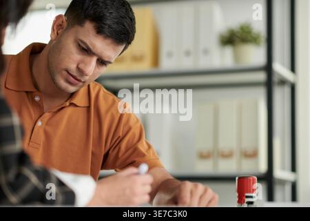 Indian man signing documents sitting in the office of social worker Stock Photo