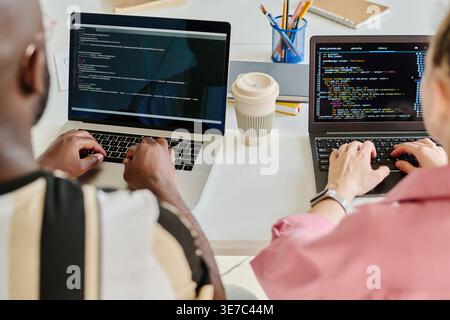 Black male and caucasian female programmers typing security codes on laptops while sitting together at table in office Stock Photo