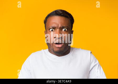Surprised Black man in white shirt standing against yellow background in studio Stock Photo