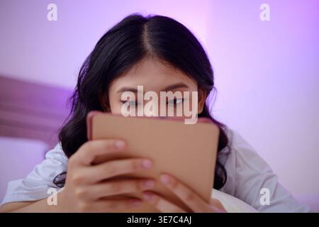 Serious Asian woman using tablet lying on bed at home Stock Photo