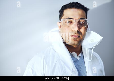 Middle Eastern male doctor wearing protective gear standing against wall in hospital Stock Photo