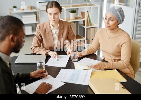 Mixed race and caucasian female HR managers discussing employment contract to male candidate during job interview in office Stock Photo