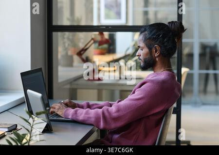 Indian male programmer working on laptop sitting at table in office Stock Photo