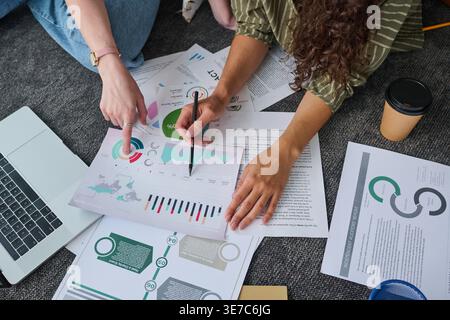 Hands of women discussing project details while sitting on floor with laptop and documents in office Stock Photo