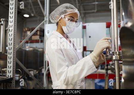 Mixed-race woman worker wearing protective mask and lab coat operating equipment in chemical factory Stock Photo