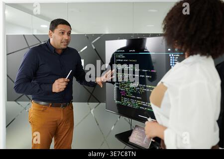 Asian man project manger and Hispanic woman developer team leader discussing programming code in big monitor screen in the office Stock Photo
