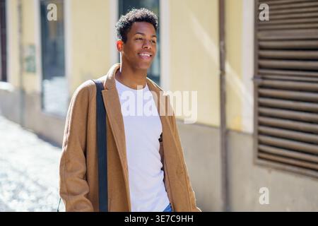 Smiling Black male walking on street on sunny day Stock Photo