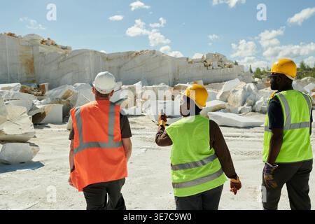 Black female and male engineer wearing safety helmets walking with caucasian male foreman in construction site Stock Photo