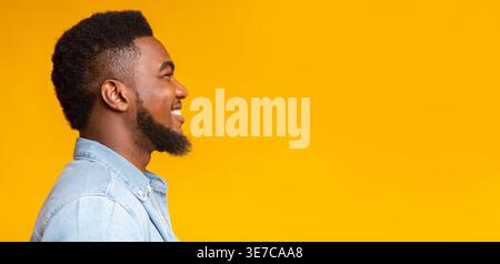 Black man with beard standing sideways against yellow background in studio Stock Photo