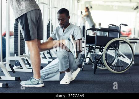 Black male therapist crouching and assisting caucasian male   doing leg exercises in physiotherphy clinic Stock Photo