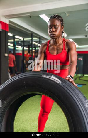 Black woman with braids doing wheel lifting exercises to strengthen quadriceps and biceps in gym Stock Photo