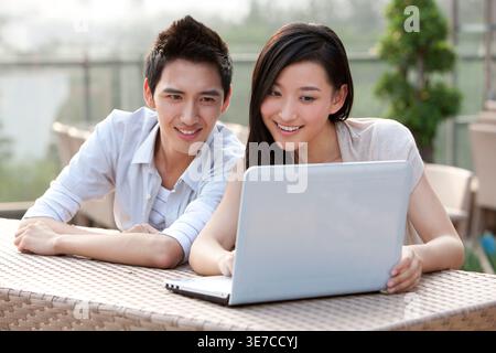 Chinese couple using laptop sitting at table in city park during daytime Stock Photo