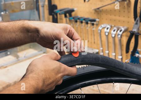 Hands of Hispanic male mechanic putting red patch on punctured bicycle tire while standing in workshop Stock Photo