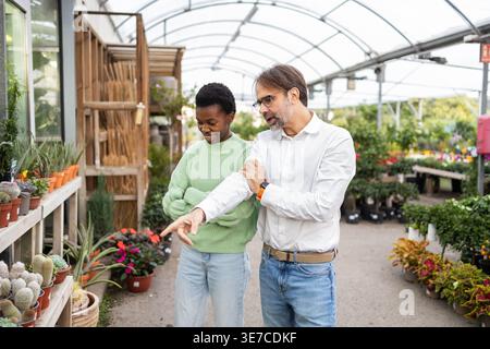 A couple explores a garden center, admiring various plants and succulents The greenhouse setting offers a wide range of greenery and colorful flowers, Stock Photo