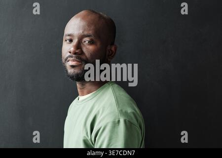 Black man with beard standing sideways against black wall at home Stock Photo