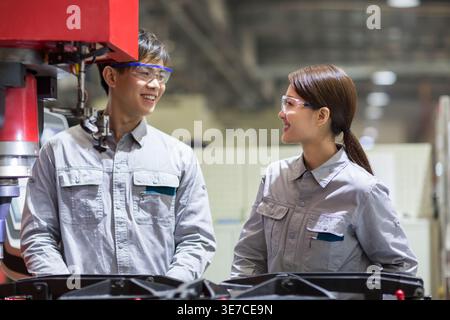 Chinese male and female engineers looking at each other talking standing near machine in fatory Stock Photo