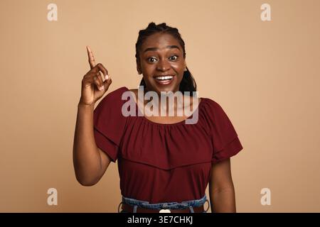 Inspired Black woman pointing finger up standing against beige background in studio Stock Photo