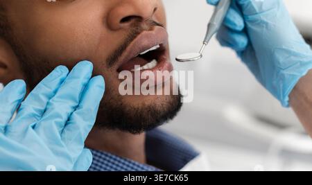 Black male patient getting his teeth checked by female dentist wearing gloves in clinic Stock Photo