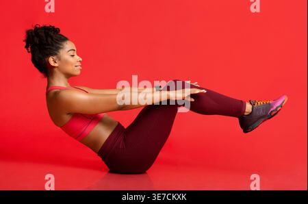 Side view of Black woman doing V-sit crunches against red background in studio Stock Photo