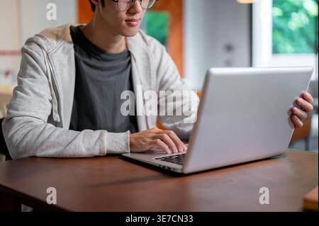 Cropped image of Asian man working on his laptop sitting at table in co-working space Stock Photo