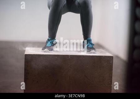 Black woman  wearing leggings and sneakers exercising doing squats on box in gym Stock Photo