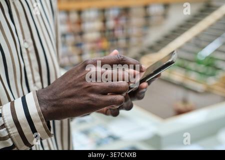Black man wearing stripe long sleeves using smartphone while standing in library Stock Photo