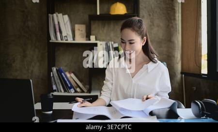 Asian middle-aged business woman reviewing documents sitting at desk in office Stock Photo