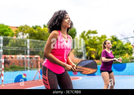 Diverse of female friends playing pickleball together in outdoor court during daytime Stock Photo