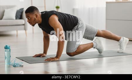 Black man looking away doing running plank exercise on yoga mat in living room at home Stock Photo