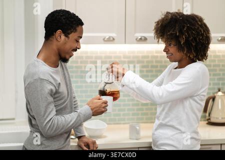 Black woman pouring coffee into cup held by husband standing near kitchen counter at home Stock Photo