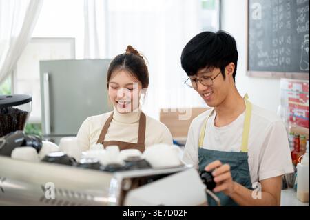 Thai male and female baristas wearing aprons preparing coffee together while standing at counter in cafe Stock Photo