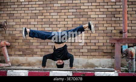 Asian male hiphop dancer in beanie doing headstand breakdancing on street during daytime Stock Photo