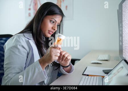 Indian female doctor showing bottle of pills video calling female colleague sitting at desk in hospital office Stock Photo