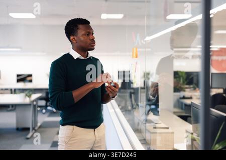 Black businessman sticking post-it notes with his ideas for new project on glass wall preparing for meeting while standing in office Stock Photo