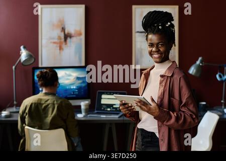 Black female office worker with braids holding tablet standing near caucasian male colleague working in office Stock Photo