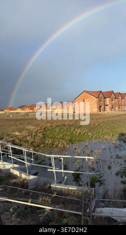 Rainbow arches over newly built brick houses beside flooded field with metal railing at Taylor Wimpey, Ripon, UK. Stock Photo