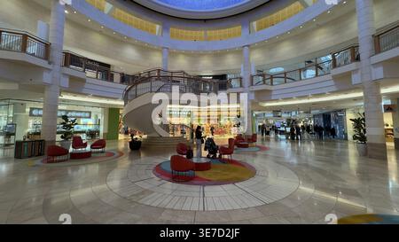 Grand circular mall atrium with spiral staircase and red chairs on patterned floor. Stock Photo