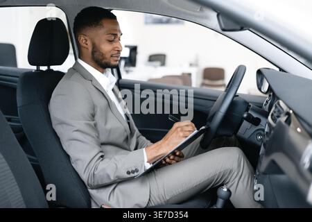 Black businessman writing notes while sitting in driver seat of car Stock Photo