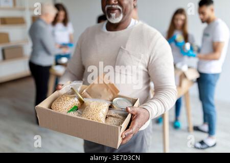 Black man carrying food donation box while standing near group of volunteers in center Stock Photo