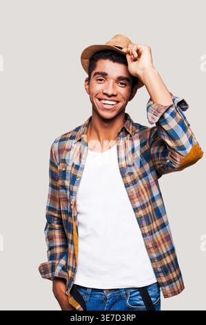 Black man tipping straw hat while standing against light gray background Stock Photo