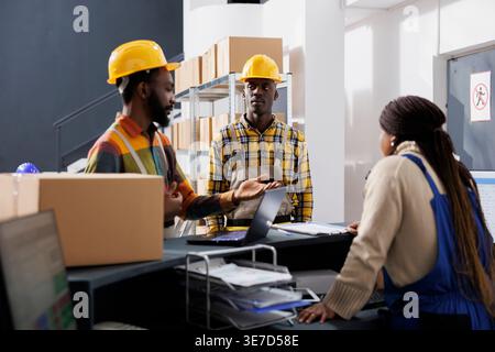 Warehouse manager explaining coworkers parcel dispatching operation at delivery service reception desk. All black shipment managers discussing package transportation at post office counter Stock Photo