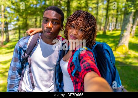 Mixed-race woman taking selfie with his Black boyfriend while standing together in forest during hiking trip Stock Photo