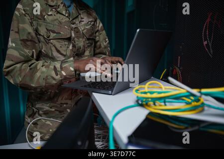 Black female soldier using laptop standing at table in server room Stock Photo