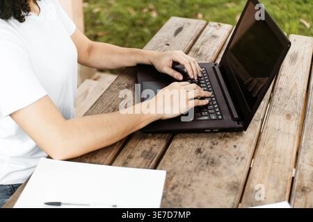 Cropped image of Hispanic woman using laptop sitting at table on campus outdoors Stock Photo