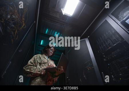 Black female soldier wearing eyeglasses using laptop while standing in server room Stock Photo