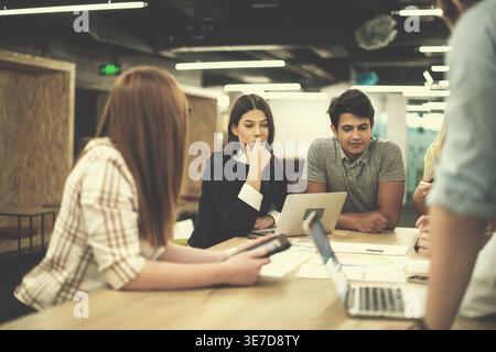 Focused diverse group of business people sitting together at table brainstorming and discussing business plans in the office Stock Photo