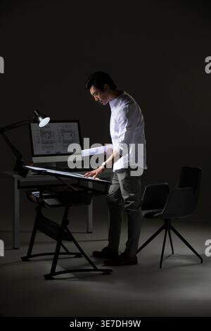Chinese male architect working on construction plan standing at table in office Stock Photo